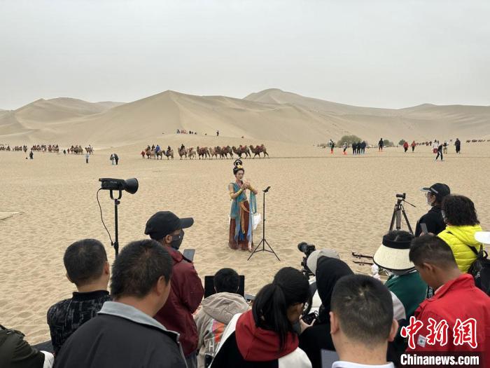 圖為2023年4月底，敦煌大漠“逐舞者”奧楠在鳴沙山月牙泉景區(qū)視頻直播，吸引游人圍觀?！●T志軍 攝