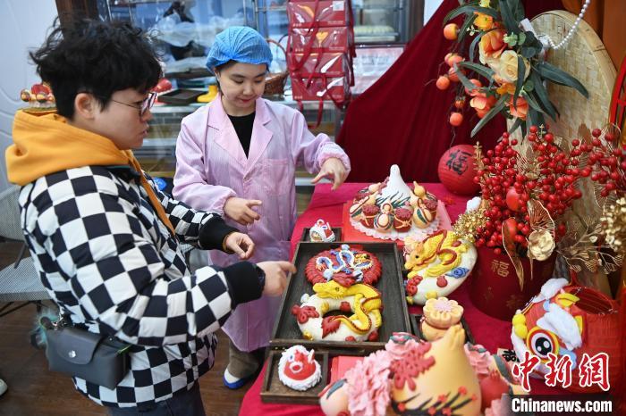 1月25日，隨著春節(jié)臨近，蘭州一花饃店“龍”元素花饃熱銷。圖為工作人員向顧客推薦“龍”元素花饃。九美旦增 攝</p><p>